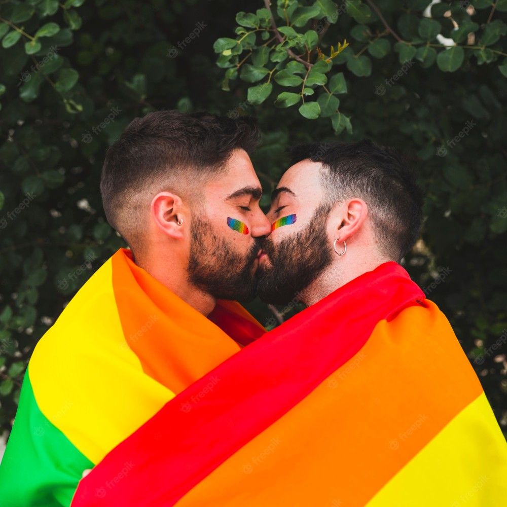 Two men embracing, wrapped in a rainbow flag